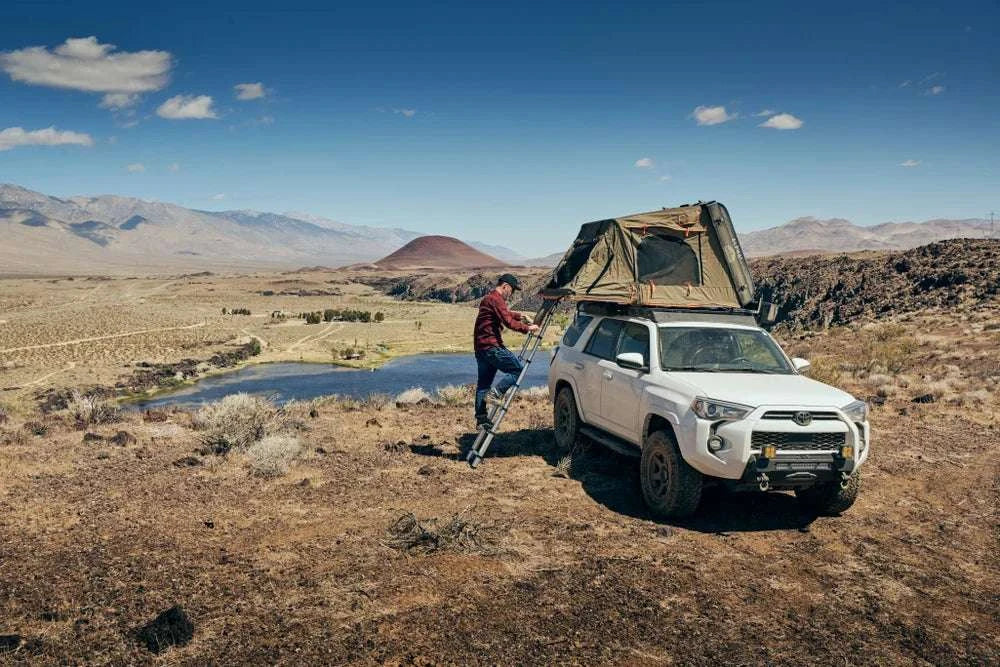 TUFF STUFF® OVERLAND ALPHA™ II hard top side open tent on SUV in a scenic outdoor setting.