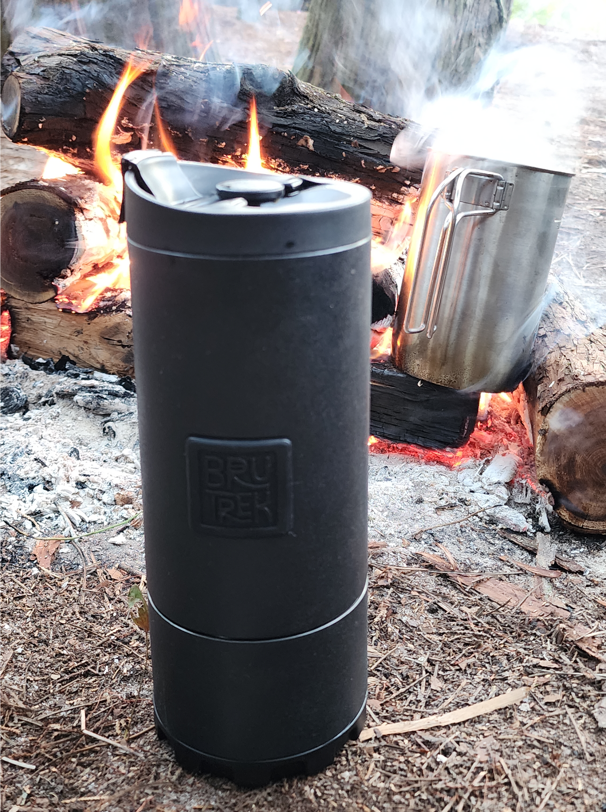 Travel Coffee Press by Ovrlndr beside campfire, rugged stainless steel design for adventure.