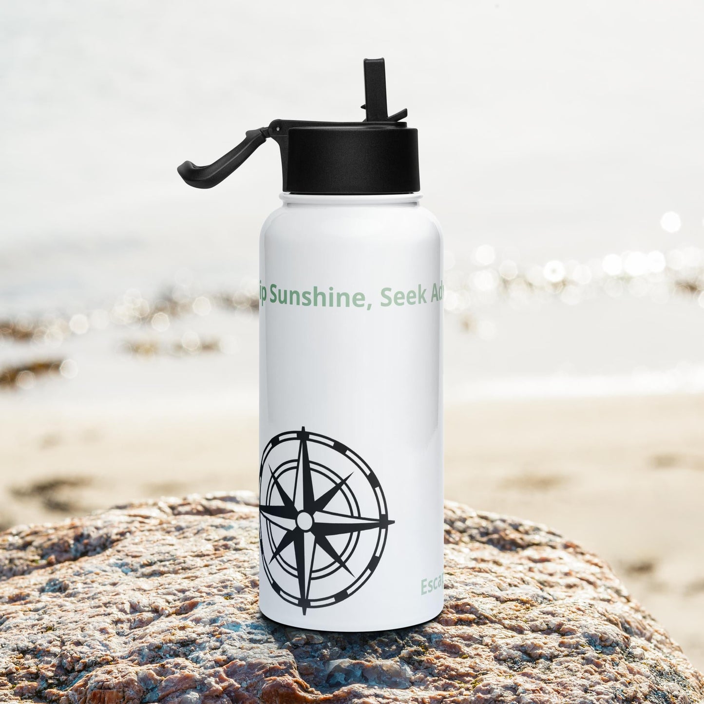 Stainless steel camping water bottle with straw lid on a rocky beach.