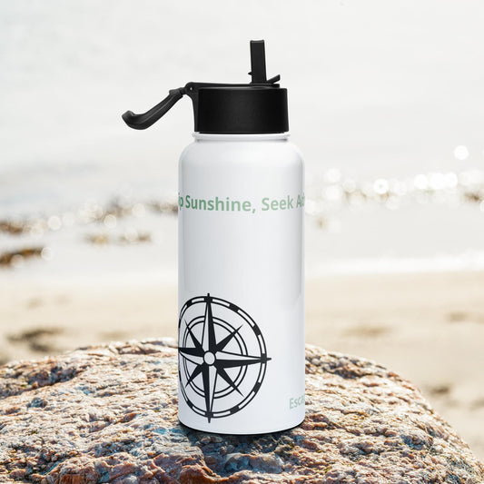 Stainless steel camping water bottle with straw lid on a rocky beach.