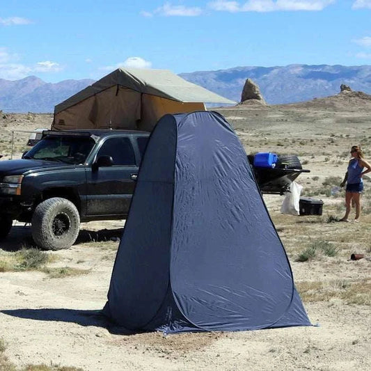 Portable outdoor changing or toilet tent set up by a vehicle in a desert landscape, offering privacy and durability for camping or trips.